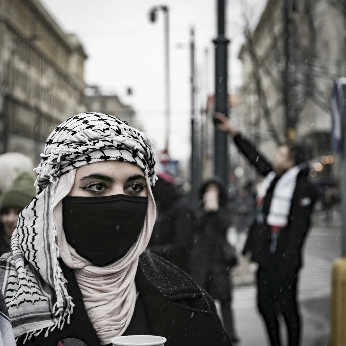 Masked person in a keffiyeh at a street demonstration